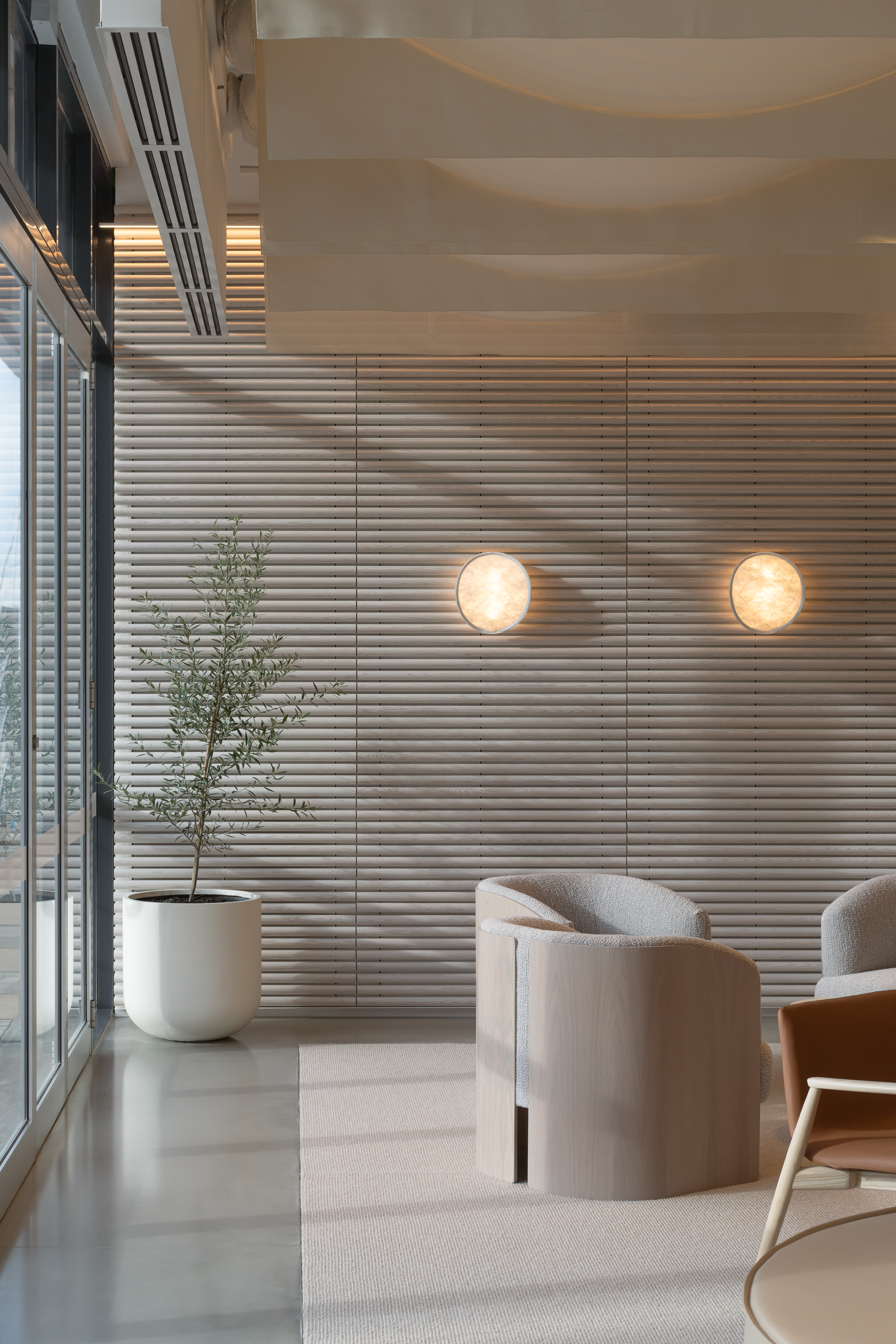 Modern interior with neutral tones, featuring armchairs, potted plant, and paneled walls, creating a minimalist and serene architectural space.