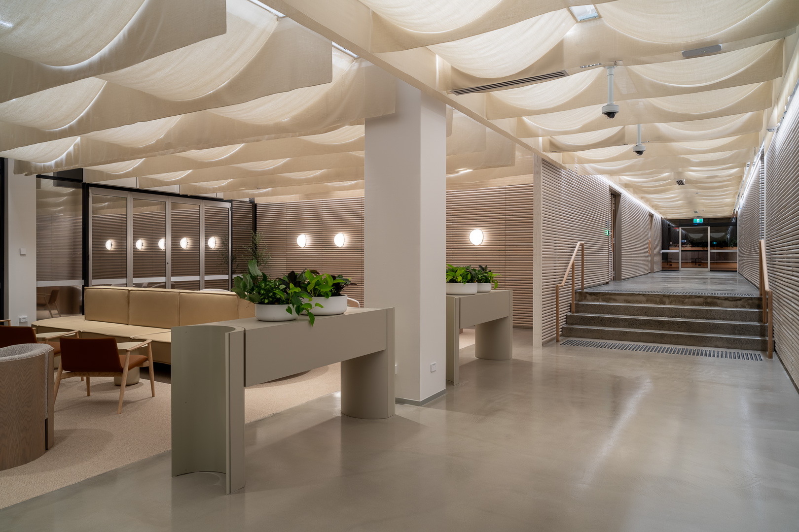 Modern interior waiting area with slatted wooden walls, polished concrete floors, and draped fabric ceiling canopy.
