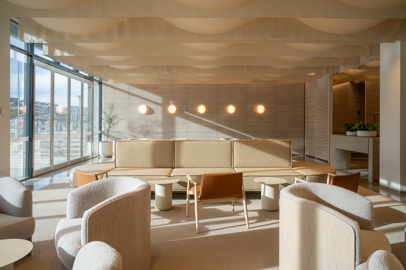Interior view of a modern waiting area with neutral-toned furniture, soft lighting, large windows, and a minimalist design aesthetic.