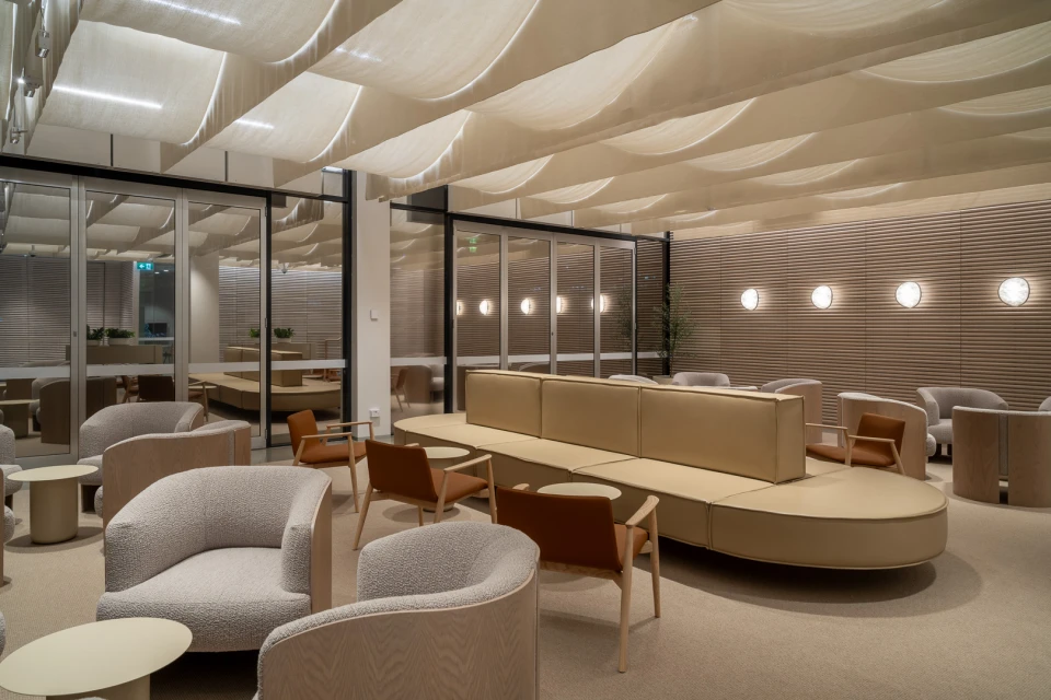Indoor lounge area featuring seating with armchairs and couches in neutral tones, complemented by modern lighting and architectural details.