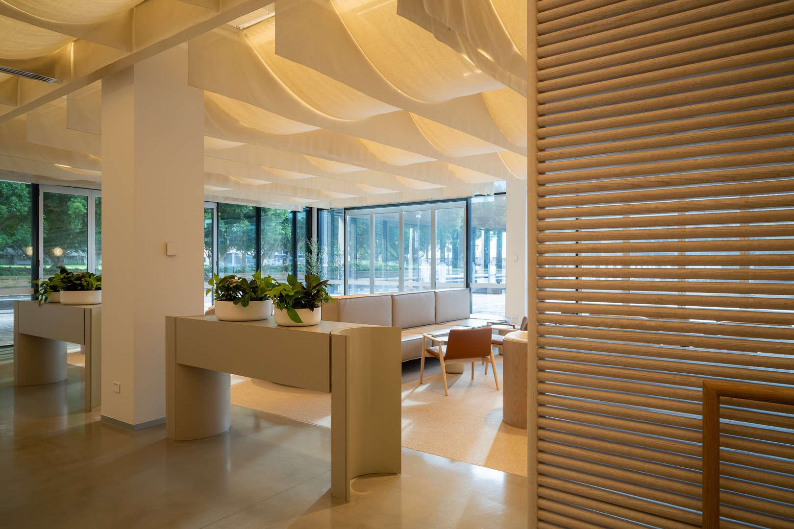 Contemporary interior design with potted plants on consoles, seating area, and unique ceiling lighting feature in a modern architectural setting.