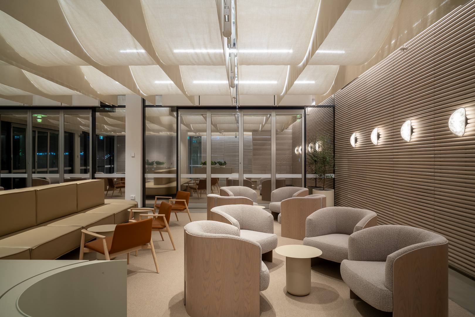 Modern interior features armchairs, sofas, and tables under a textured ceiling with lighting in an inviting neutral color palette.