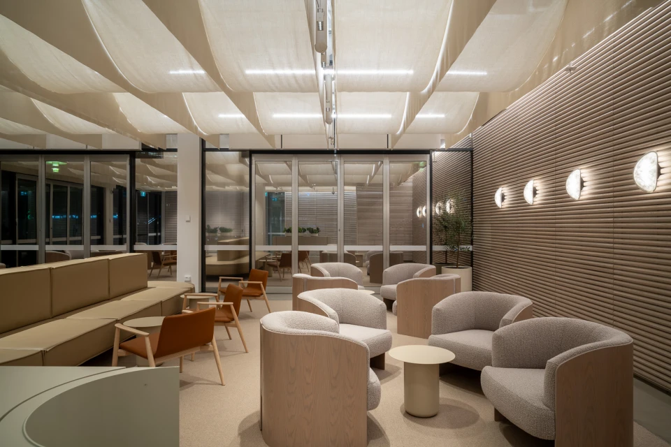 Modern interior features armchairs, sofas, and tables under a textured ceiling with lighting in an inviting neutral color palette.