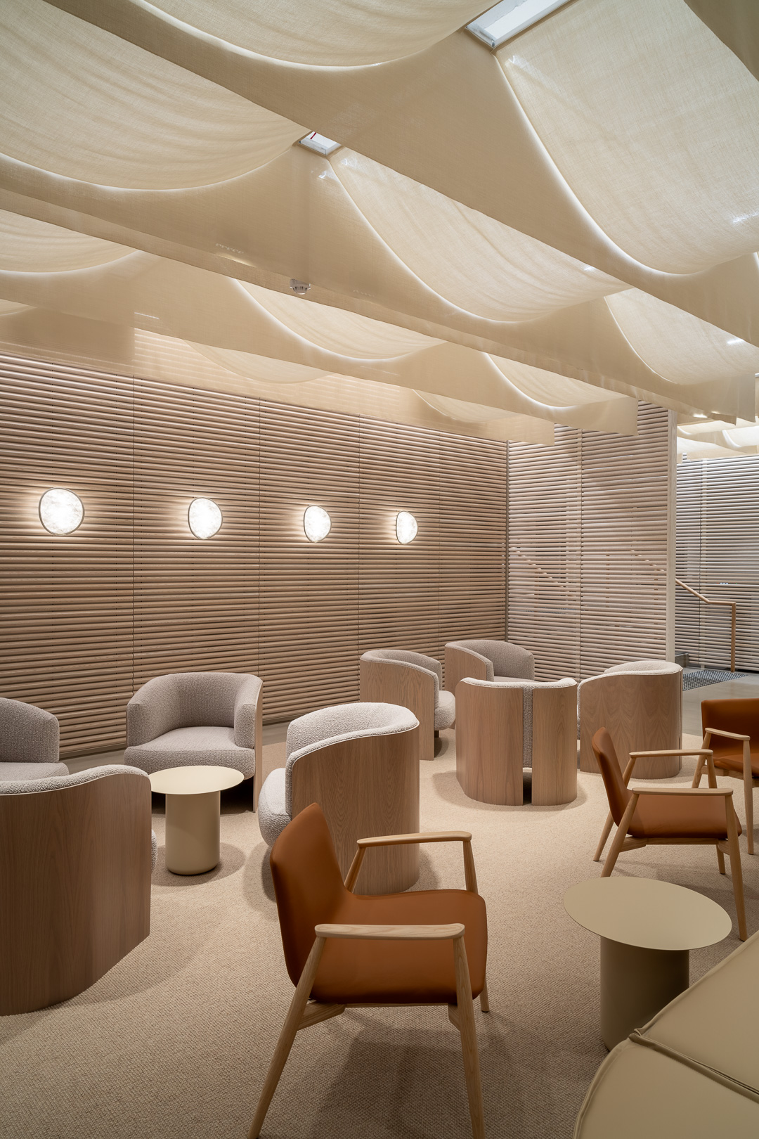 Interior space showcasing seating area with armchairs and small tables, featuring soft lighting and neutral tones, and a fabric-covered ceiling.