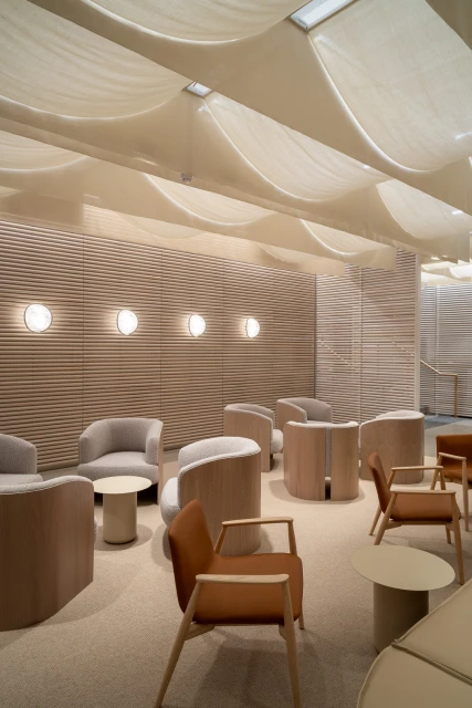 Interior space showcasing seating area with armchairs and small tables, featuring soft lighting and neutral tones, and a fabric-covered ceiling.