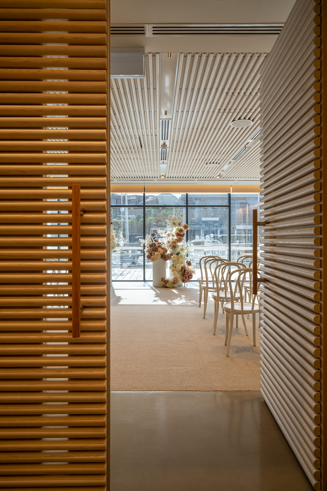 View through partially opened wooden doors to an interior space set up with white chairs and floral arrangements.