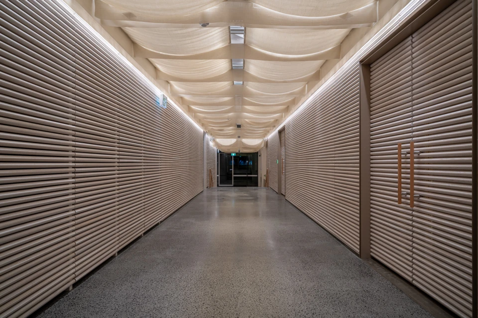 Indoor shot of a long hallway with light grey walls with parallel lines, a patterned ceiling, and a light grey speckled floor.