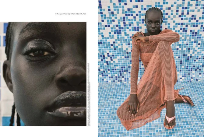 Fashion shot of a black woman in a peach-colored, net dress and sandals, seated in front of a blue mosaic tile wall with neutral expression.