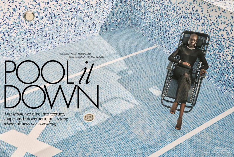 Fashion shot of an African woman in a black dress reclining on a chair in a blue and white tiled swimming pool, shot at eye level.