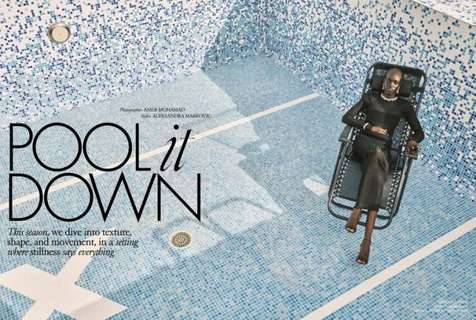 Fashion shot of an African woman in a black dress reclining on a chair in a blue and white tiled swimming pool, shot at eye level.