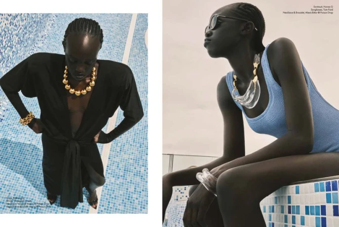 Two dark-skinned women pose in swimwear and statement gold jewelry near a blue-tiled pool, showcasing fashion and elegance in a bright setting.