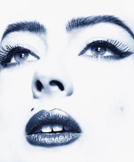 Close-up portrait of a woman's face in monochrome with dramatic eyelashes, defined eyebrows, and glossy lips, focusing on beauty and makeup.
