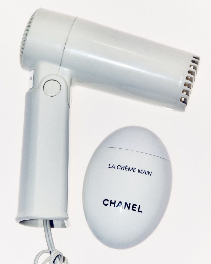 Elevated product shot showcasing a white hair dryer and a Chanel hand cream on a clean white background, highlighting their design and form.