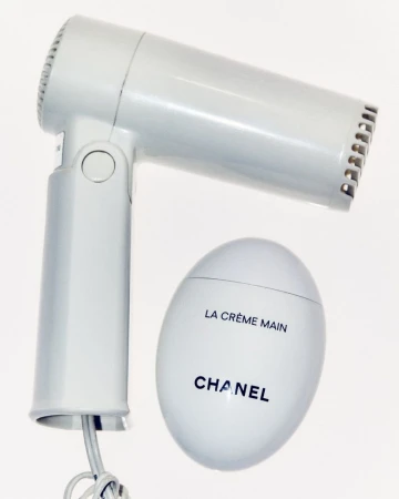 Elevated product shot showcasing a white hair dryer and a Chanel hand cream on a clean white background, highlighting their design and form.