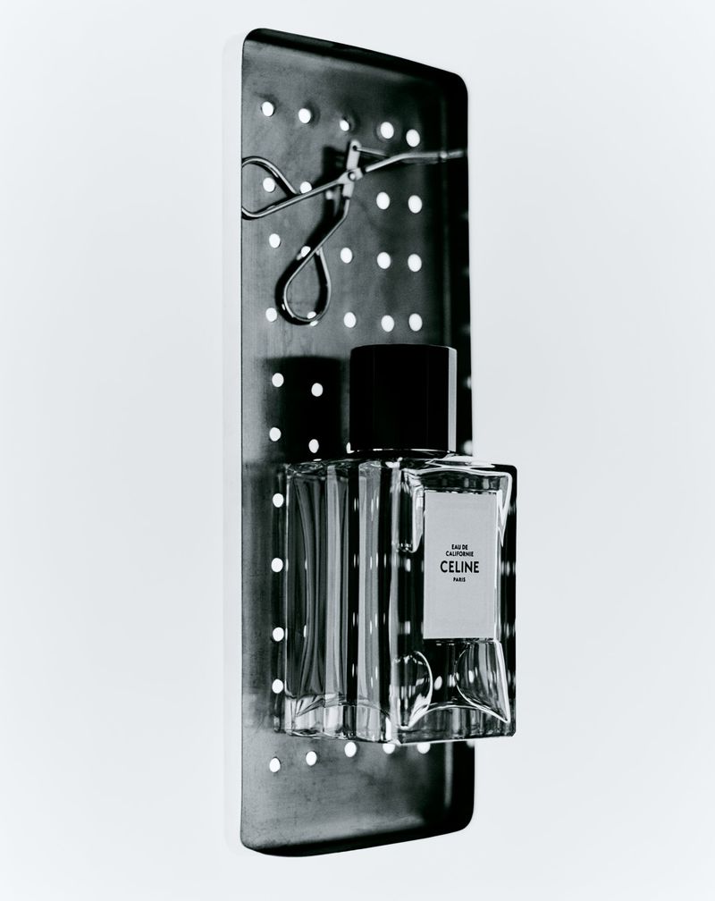 Celine Paris perfume bottle on a metal stand with metal eyelash curler on a white background in a studio shot.