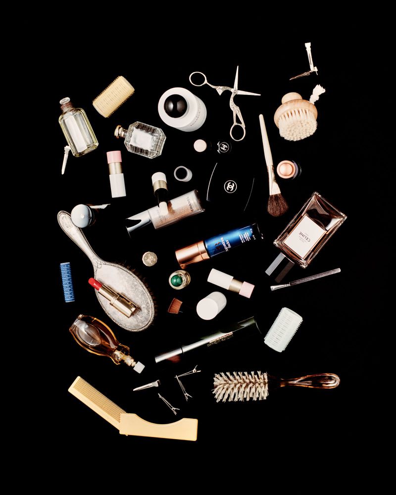 Flat lay of various beauty and grooming products arranged against a black background, including perfumes, brushes, and hair accessories.