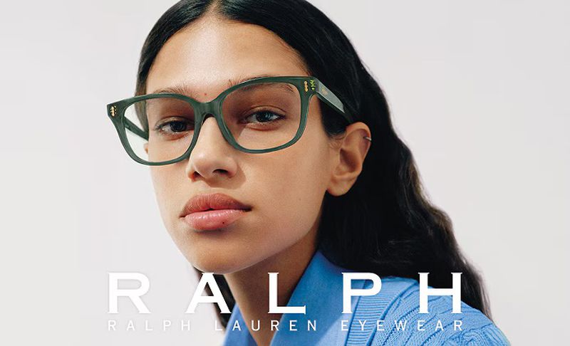 Close-up of a brunette woman wearing green Ralph Lauren eyeglasses in a fashion shot against a white backdrop.