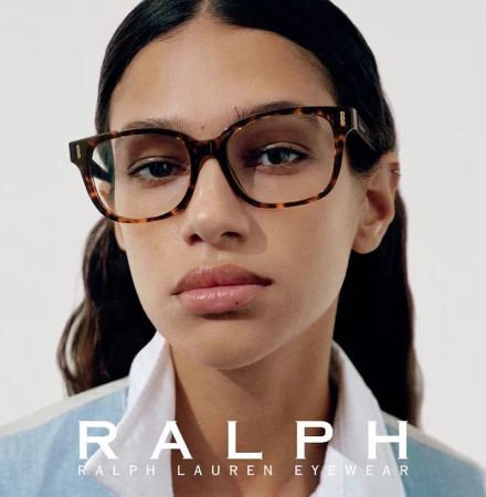 Close-up studio portrait of a brunette female model wearing tortoise shell Ralph Lauren eyewear and a light blue shirt.