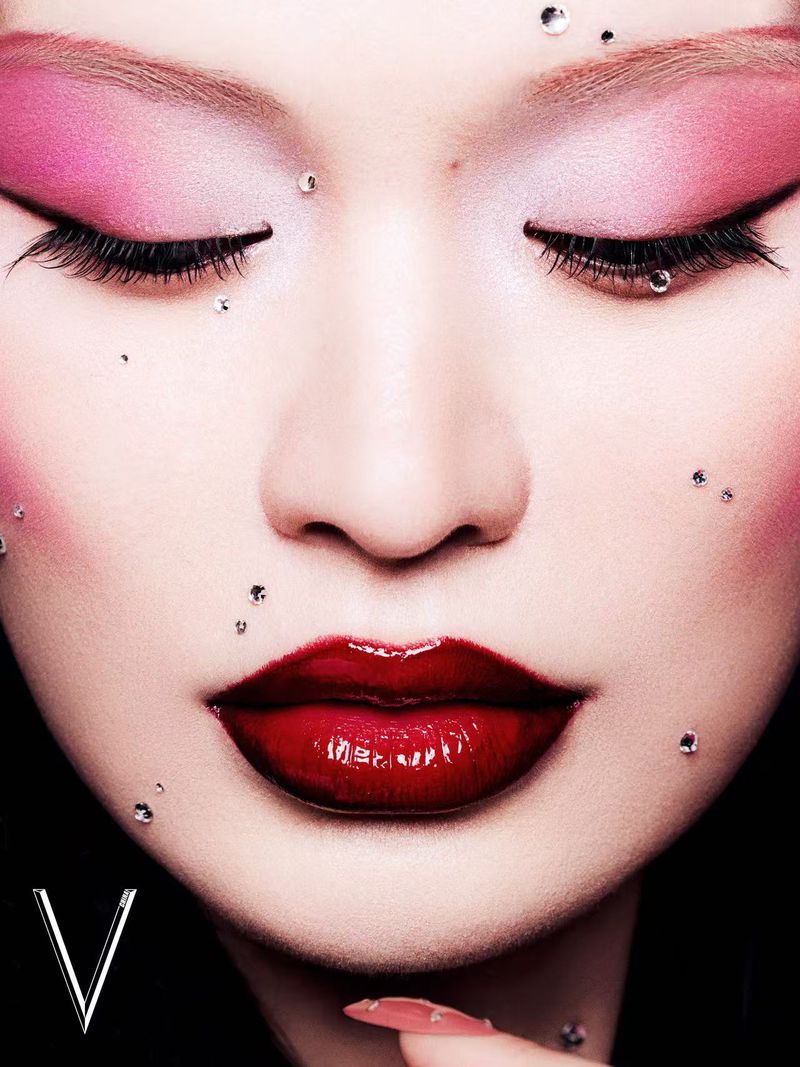 Close-up of a woman's face with pink eye shadow, red lips, and small gems around her eyes. Beauty and makeup concept for fashion or beauty.