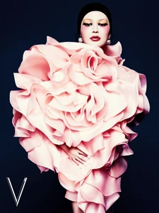 Model wearing a massive sculpted pink ruffled floral dress with a black cap against a dark background