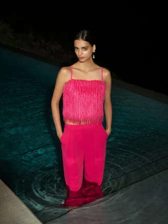 Woman in pink fringe top and pants standing in pool at night. Fashion shot with dark, moody lighting, and serene poolside environment.