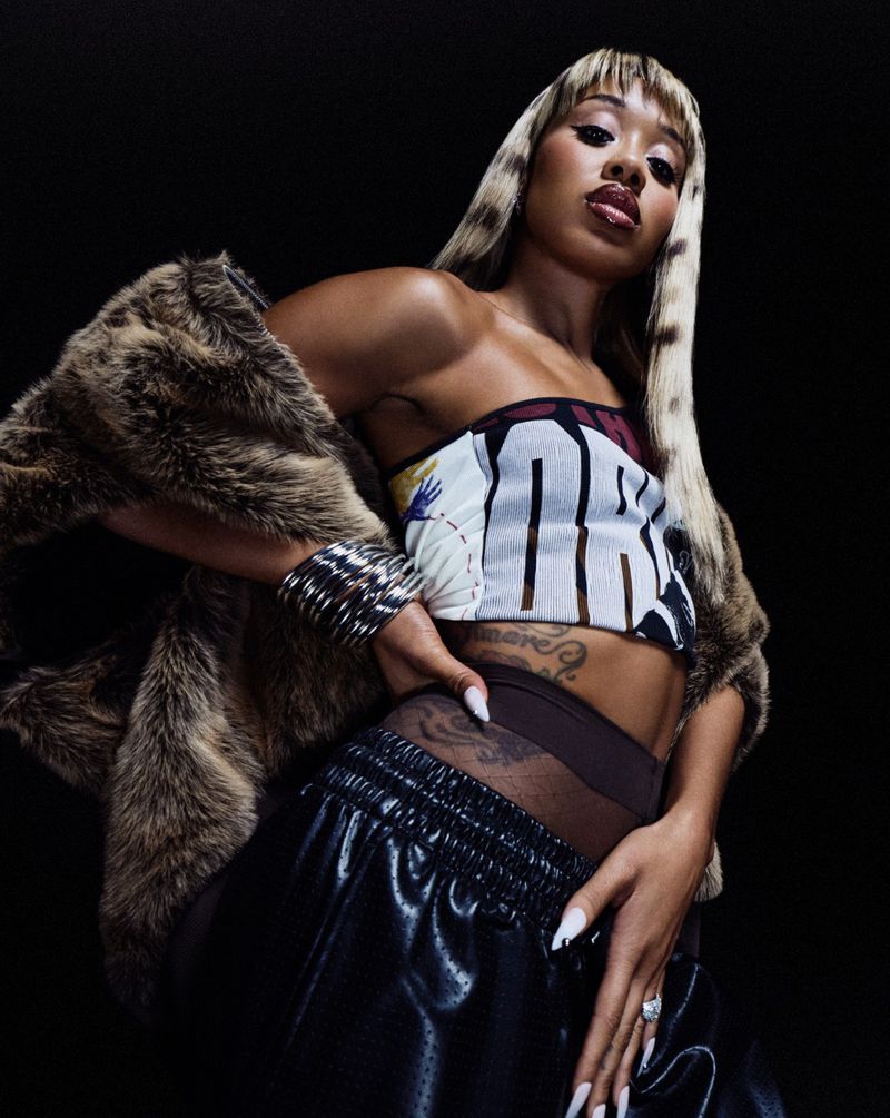Portrait of a woman wearing a printed top, fur coat and sweatpants against a dark backdrop, showcasing fashion and personal style.