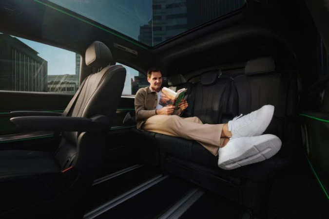 Man relaxes in a luxury vehicle, reading a book, with a city view visible through the sunroof. Interior shot with leather seating.