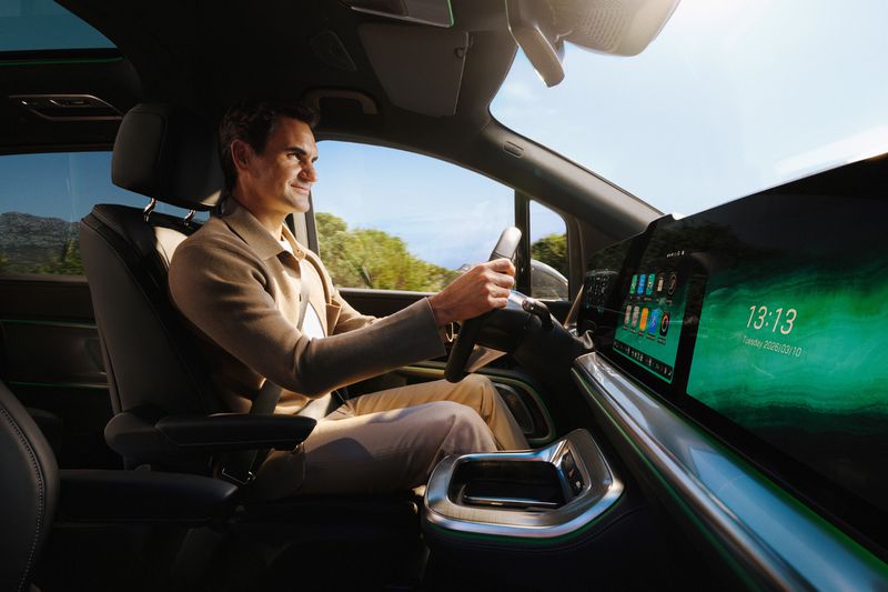 A man in a tan suit is driving an electric vehicle with a large digital display showing the time as 13:13 and the date as Tuesday, 2026/03/10.