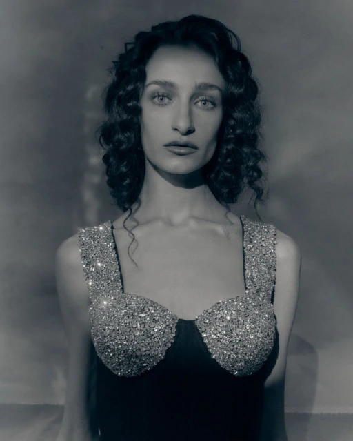Monochrome portrait of a woman with curly hair, wearing a sparkling bodice, against a blurred background in a studio shot.
