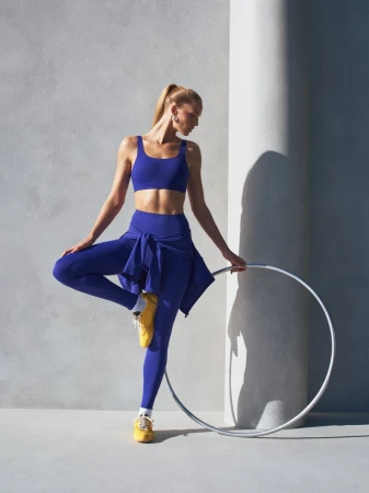 Model in blue athletic wear holding a hula hoop against a concrete architectural backdrop
