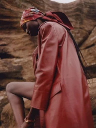 Model Amam Abit in a red leather coat and headscarf posing on rocky terrain for Blanc Magazine.