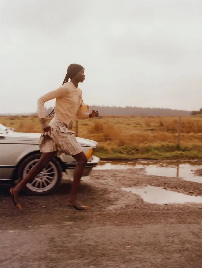 Model Amam Abit running past a silver car on a dirt road for Blanc Magazine photographed by Oliver Oglesby