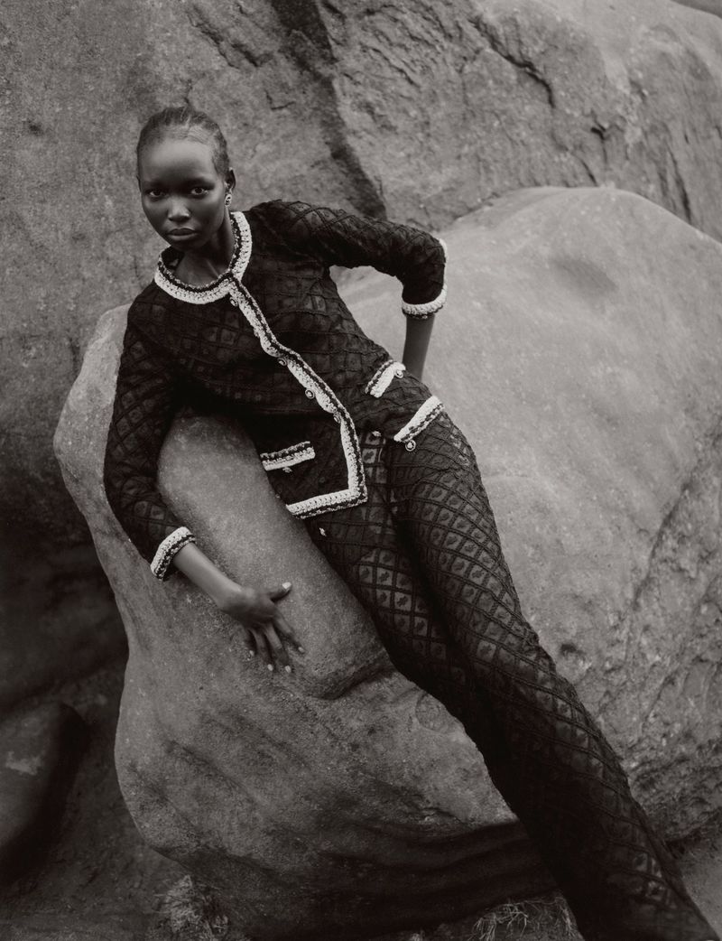 Model Amam Abit posing against large rocky boulders wearing a textured black patterned suit for Blanc Magazine.