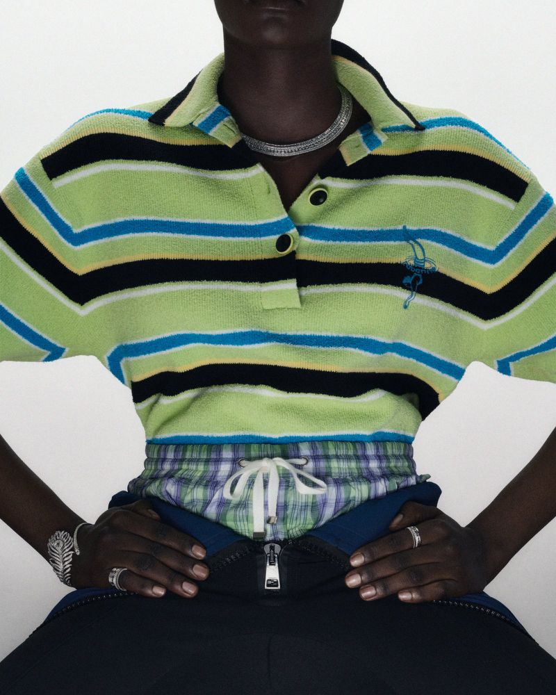 Fashion shot: Model wearing a striped polo shirt, plaid shorts, and open dark blue pants against a white backdrop in a studio setting.