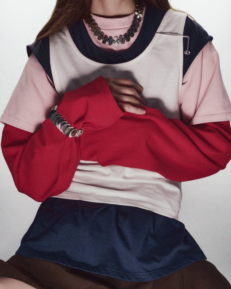 Model presents fashion with a layered t-shirt, dark skirt, silver necklace, and bracelet in a studio setting. Fashionable and stylish.