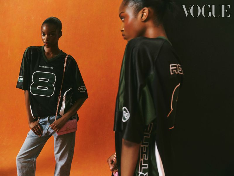 Two Black fashion models pose against a split orange-black background wearing matching jerseys and jeans for a Vogue magazine editorial.