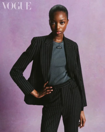 Model in a black pinstripe suit and grey crewneck t-shirt posing against a textured purple background for British Vogue