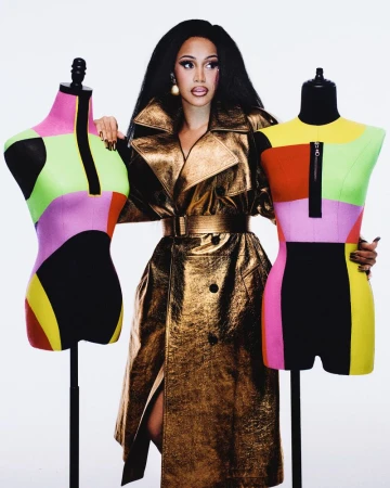 Portrait of adult female celebrity wearing metallic trench coat with black hair posing with colourful mannequins in a white studio setting.