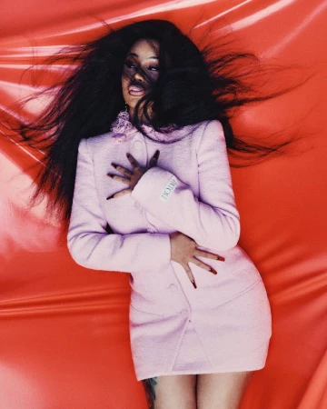 Cardi B wearing a pink jacket and skirt with long dark hair against a glossy red background for Allure.