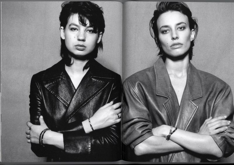 Black and white portrait of two adult women, side by side, with serious expressions and arms crossed, wearing jackets in a studio.