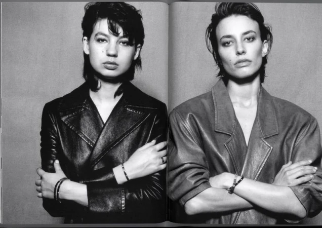 Black and white portrait of two adult women, side by side, with serious expressions and arms crossed, wearing jackets in a studio.