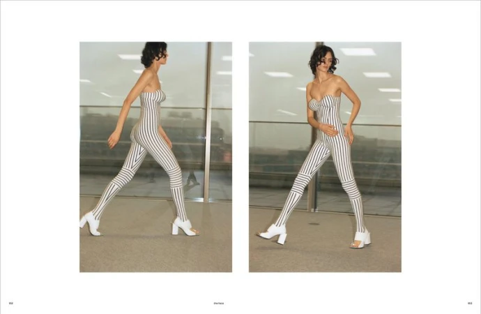 A slender woman models a full-body striped strapless garment and white block-heeled shoes in a minimal indoor setting with natural light.