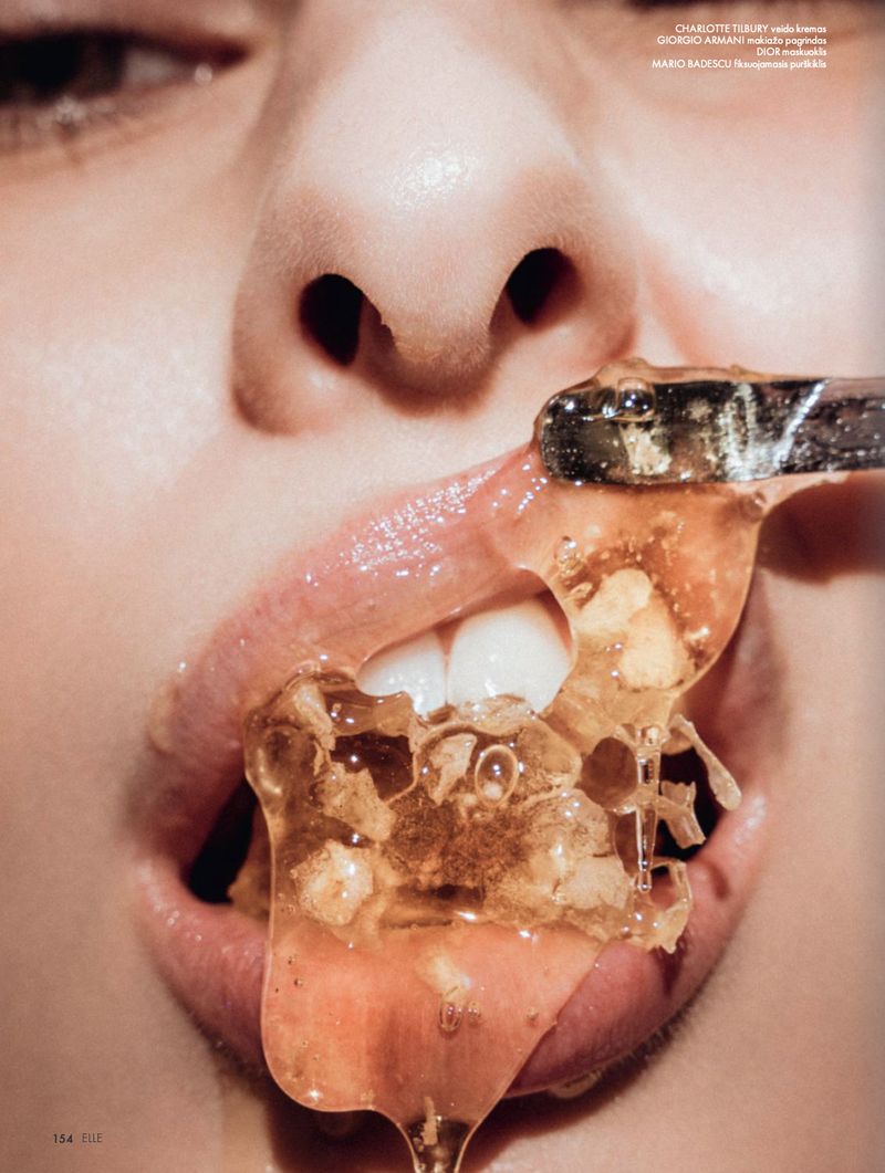 Extreme close-up shot of a person's mouth with honey on a silver utensil, teeth, and face, under neutral lighting, in studio setting.