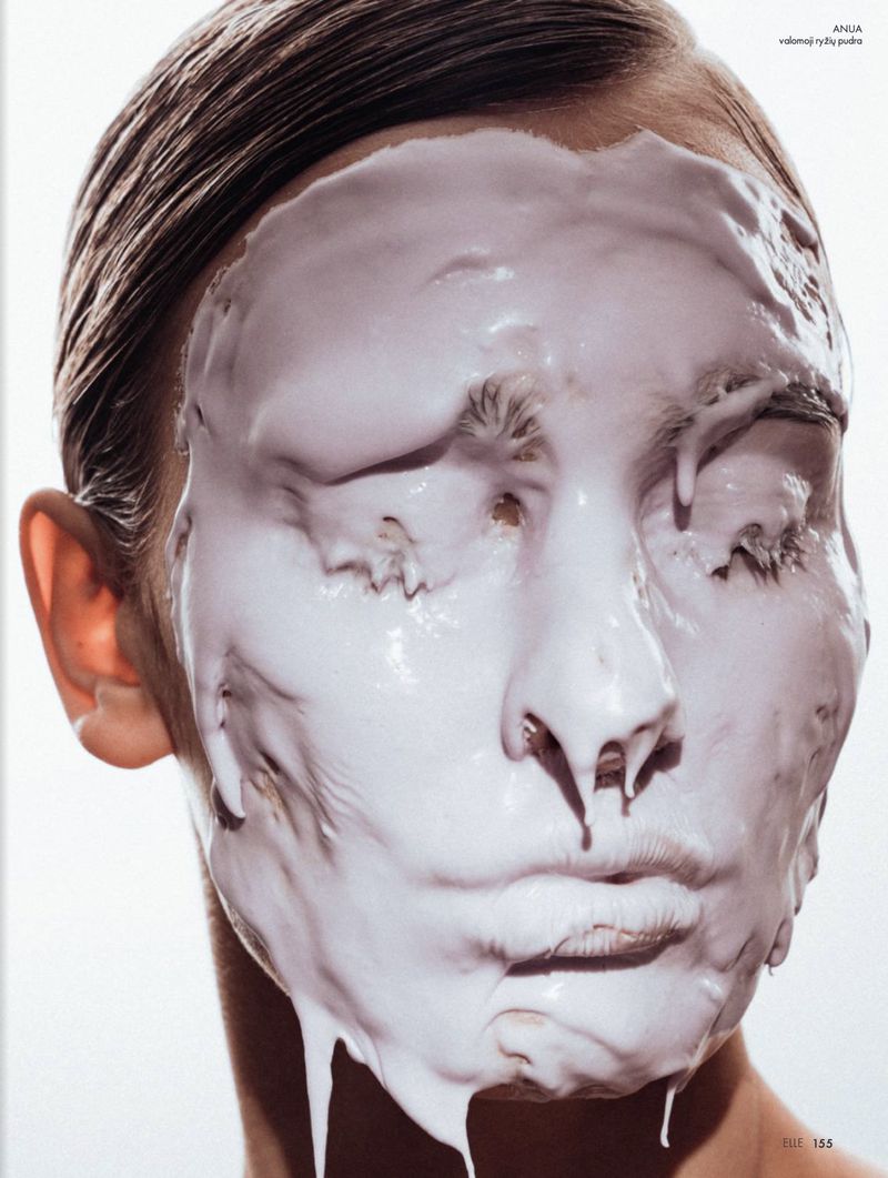 Close-up portrait of a fair-skinned adult woman with closed eyes, partially covered in a thick, white substance in a studio setting.