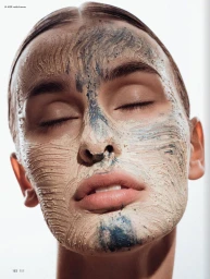 Close-up portrait of a woman with her eyes closed, wearing a textured clay skincare mask across her face.