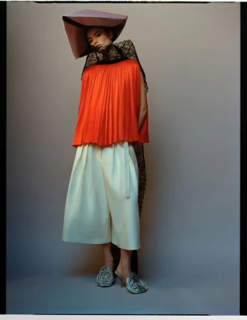 Fashion shot of a stylish woman in a square hat, red top, and white pants, posing against a neutral background, creating a visually striking image.