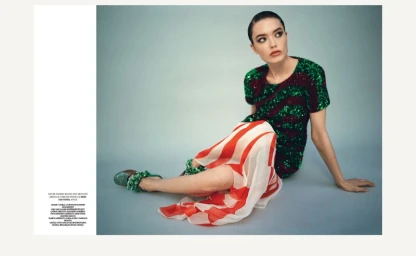 Model seated on a grey seamless studio floor wearing a green and burgundy sequined top and a red and white striped skirt
