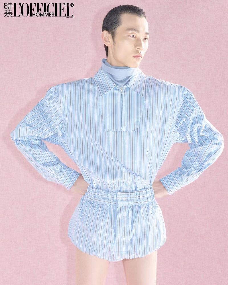 Asian male model in blue striped shirt and short-shorts posing in front of a pink background for L'Officiel Hommes magazine.