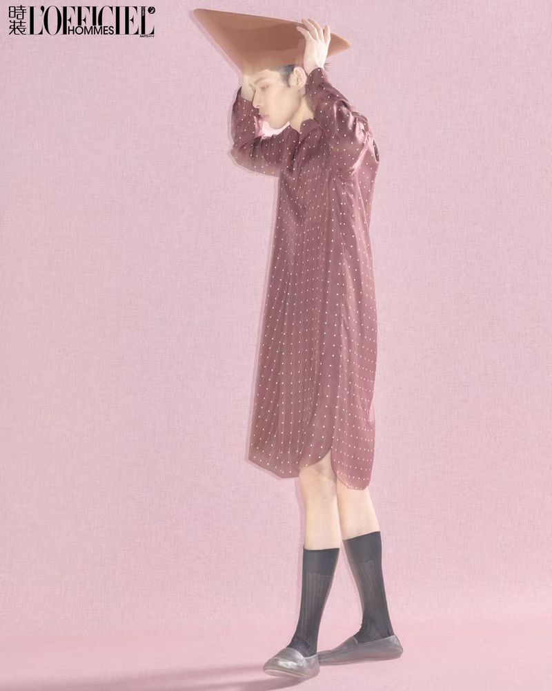 Stylish full shot of a slender Asian man in an oversized dotted shirt, sheer socks, and silver shoes, posing in a pink studio.