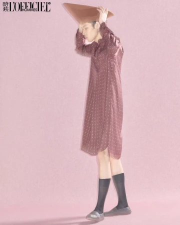 Stylish full shot of a slender Asian man in an oversized dotted shirt, sheer socks, and silver shoes, posing in a pink studio.